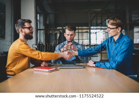 Unsociable hipster guy overuse mobile phone ignoring real communication while his male colleagues shaking hands during meeting, agreement and congratulation, problem of millennial internet addiction