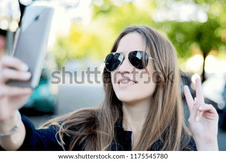 Portrait of a young beautiful woman taking selfie with her smartphone. Outdoors.