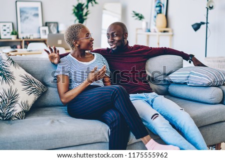 Positive african american couple in love sitting on comfortable couch having conversation about relationships,young dark skinned family resting at home together communicating at living room  Royalty-Free Stock Photo #1175555962