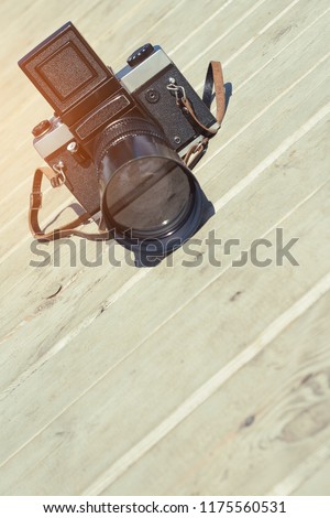 The retro camera is located on the wooden surface of the boards in the sunlight. Vertical frame. Medium format camera with a shaft and leather strap. Reflection in the camera lens. Selective focus.