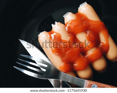 Top view picture of sausage on top with ketchup above black texture.