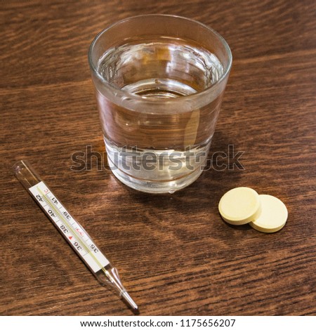 A glass with water, tablets and a thermometer on the table