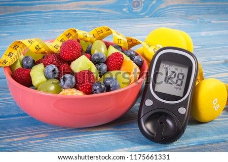 Fruit salad, glucose meter with result of sugar level, tape measure and dumbbells for fitness, concept of diabetes, sport, diet, slimming, healthy lifestyles and nutrition Royalty-Free Stock Photo #1175661331