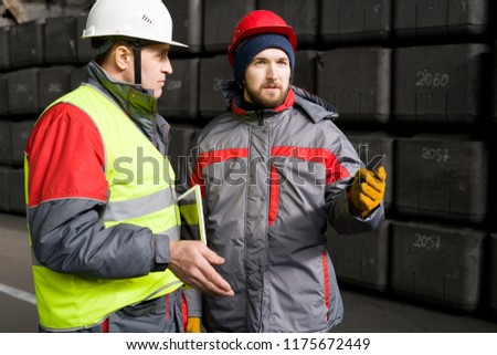 Waist up portrait of factory worker wearing hardhat  taking to foreman while standing in workshop