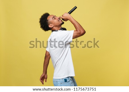 Young handsome African American Male Singer Performing with Microphone. Isolated over yellow gold background. Royalty-Free Stock Photo #1175673751