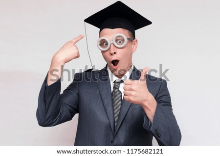 Graduate student is showing on his graduation cap and showing a thumbs up isolated on gray background. Education concept.