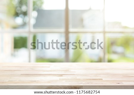 Wood table top inside the house with sunlight shining through window and blur green garden as background, can be used for display and montage your products or food