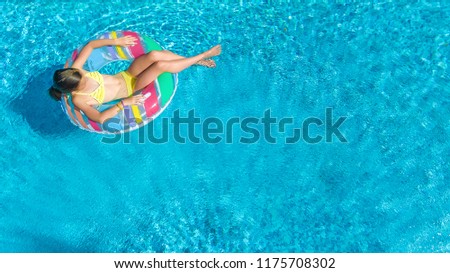 Aerial drone view of little girl in swimming pool from above, kid swims on inflatable ring donut , child has fun in blue water on family vacation resort