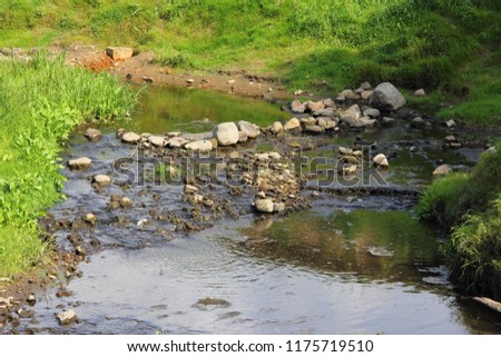 Rocky winding bed of a small river in the summer day against the green banks of the valley