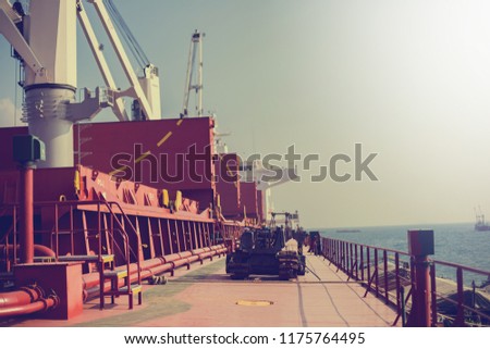 Tractor on cargo ship with bucket and crane for loading. Shipment from a merchant ship to a small ship. Grapple crane fill into cargo ship.