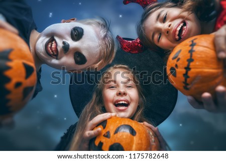 Happy brother and two sisters at Halloween. Funny kids in carnival costumes outdoors. Cheerful children and pumpkins buckets on night sky background.