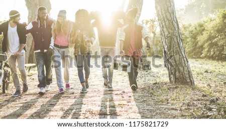 Happy generation z friends walking in city park on fall time - Young people having fun listening music and laughing together - Youth and millennials lifestyle concept - Focus on center feet