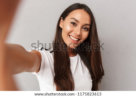 Image of excited happy young woman isolated over grey background make selfie by camera. Royalty-Free Stock Photo #1175823613