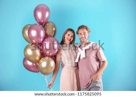 Young couple with air balloons on color background
