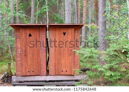 Two wooden public outdoor toilet cabins in park or forest installed for tourists male female sign. 
