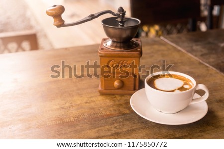 A white cup of coffee and coffee grinder on wooden table in the morning for coffee concept