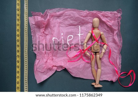 Sheet of crumpled paper with word DIET, measuring tapes and small mannequin on dark background