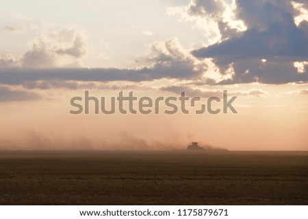 the tractor harvests by raising clouds of dust at sunset