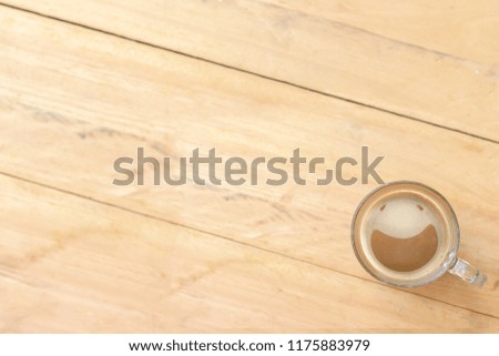 Top view picture of clear glass coffee cup with smiling face from creamy coffee froth put on the mirror table and blurry wooden textured floor background. Selective focus and copy space.