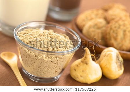 Powdered Maca or Peruvian ginseng (lat. Lepidium meyenii) in glass bowl with milk, chocolate drink, maca cookies and maca roots (Selective Focus, Focus one third into the maca powder) Royalty-Free Stock Photo #117589225