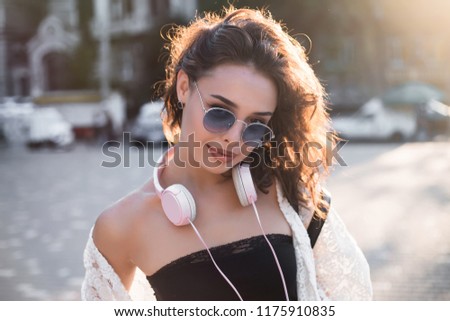 Close up image of happy brunette woman in sunglasses and autumn clothes posing sideways outdoors.Happy woman in sunglasses and dress walking outdoors. Looking at camera.Summer