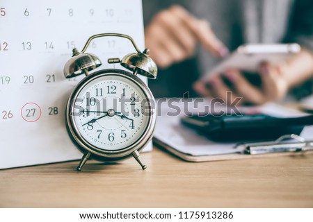 due date calendar and alarm clock with blur business woman hand calculating  monthly expenses during tax season. Royalty-Free Stock Photo #1175913286