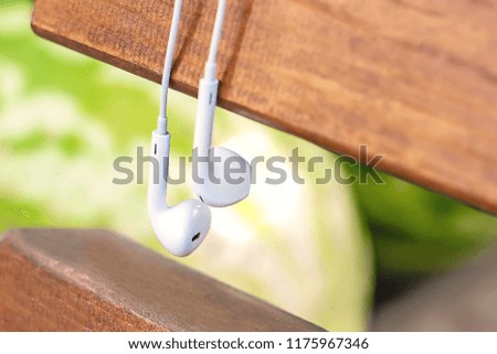 Little white earphones hang on the bench. The concept of technology and nature