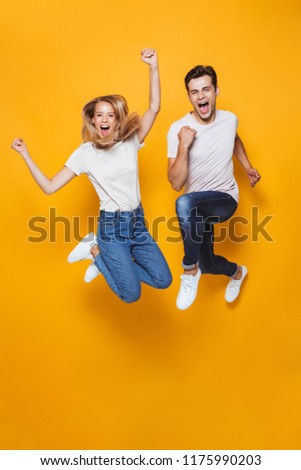 Photo of happy excited young loving couple jumping isolated over yellow wall background.