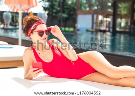 Modern smartphone. Nice joyful woman fixing her glasses while holding her mobile smartphone