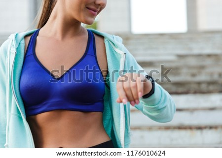 Cropped photo of amazing young sports woman standing outdoors using watch clock.