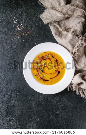 Plate of vegetarian vegan pumpkin carrot soup decorated by balsamic vinegar and thyme served with chili pepper, salt and cloth over black texture background. Flat lay, copy space