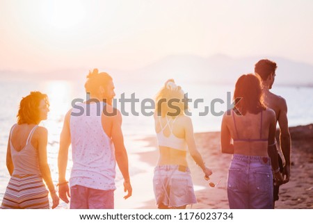 Group of young men and women walking on sandy beach and looking happy.