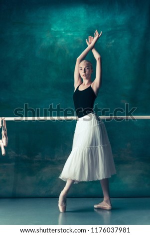 The classic ballet dancer in white tutu posing at ballet barre on studio background. Young teen before dancing. Ballerina project with caucasian model. The ballet, dance, art, contemporary