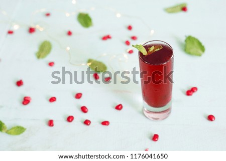 A glass of fresh pomegranate juice with pomegranate seeds and mint leaves on wooden table