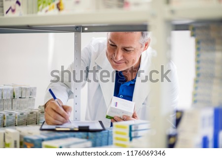 Male pharmacist checking medicines inventory at hospital pharmacy. Pharmacist in drugstore or pharmacy taking notes. Portrait of health care doctor in pharmacy writing on clipboard
