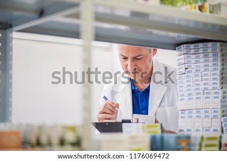 Male Chemist Arranging Stock In Shelves At Pharmacy. Male pharmacists working in warehouse depot. Man worker in pharmacy company warehouse. Horizontal view of pharmacist working in pharmacy
