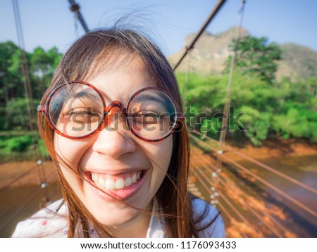 A women wearing glasses and having beautiful smile stands  on the bridge in good weather with mountain background , surat thani province in thailand