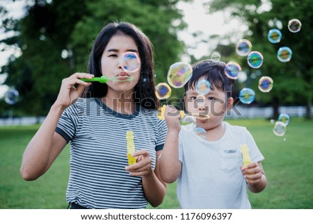 Happy Mother and child outdoor playing with soap bubble on meadow.