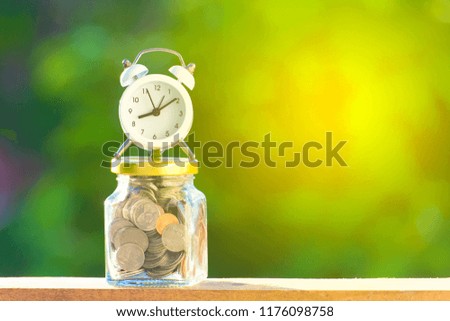 Golden and silver with closed bottle coin with white alarm clock on beautiful natural green background. investing and financial saving currency concept. vintage style.