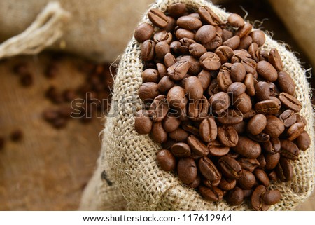Roasted coffee beans in jute sack on wooden background