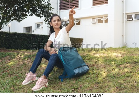 Teenager woman in jean,white t-shirt and solar glasses sit on grass,outdoor and building behind. 