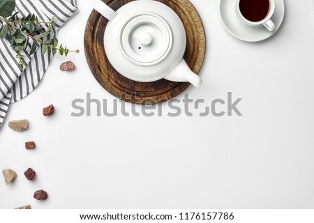 A white porcelain teapot on a wooden board and a white cup with tea on a table. Top view. Copy space. Royalty-Free Stock Photo #1176157786