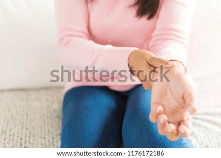 Closeup woman sitting on sofa holds her wrist hand injury, feeling pain. Health care and medical concept.