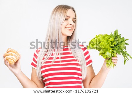 Portrait of a confused beautiful young blonde woman choosing between a healthy and unhealthy food. Isolated over white background.  