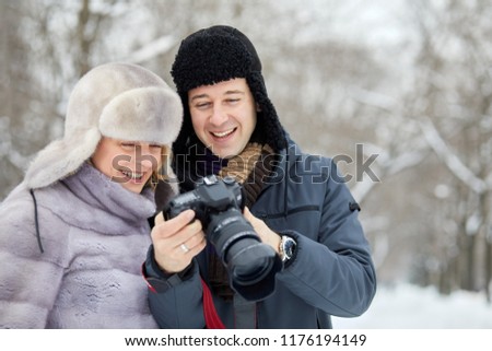 Smiling man and woman look at display of camera in winter park.