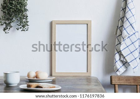  Stylish interior design of kitchen space with small table with mock up frame, herbs, cups of tea and eggs. Minimalistic interior.