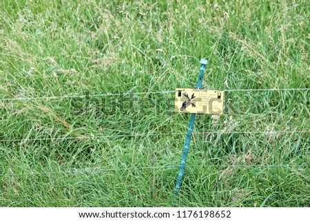 Electrified fencing with warning sign on a grass turf.
