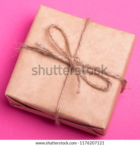 А gift in a kraft wrapper, tied with string on a pink yellow background. A corporate present.
