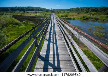 a woman is standing on a bridge across a small river in the countryside. an old wooden bridge stretching into the distance.