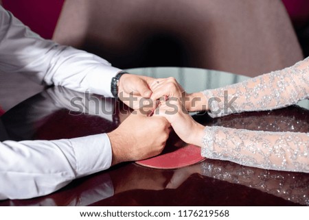 man is holding woman hands. young guy in white shirt,  girl in an evening dress are sitting at the table. concept of relationship